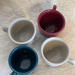 May include: Four ceramic mugs in different colors: white, teal, gray, and burgundy. The mugs are all the same size and shape, and they have a simple, modern design.