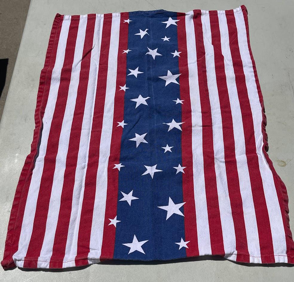 May include: A rectangular towel with a patriotic design. The towel features alternating red and white vertical stripes, with a blue central panel adorned with white stars. The towel is made of a soft, absorbent material.