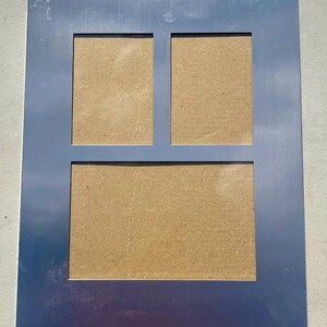 May include: A rectangular, multi-photo frame with a brushed silver finish. The frame has three openings: two smaller ones at the top and a larger one below. The backing is a light brown color.