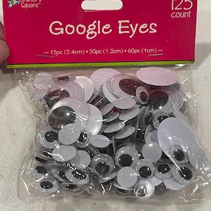 May include: A clear plastic bag filled with googly eyes of various sizes. The package has a pink and green label with the words "Google Eyes" and "Crafter's Square". The label also indicates a count of 125 eyes.