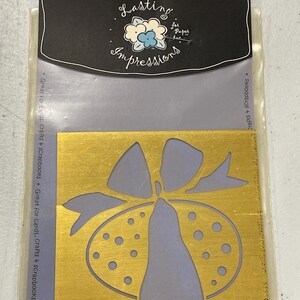 May include: A gold-colored embossing template with a bow and bell design. The template is in a clear plastic package with the text "Embossing Template" and "Lasting Impressions". The package is designed for cards, crafts, and scrapbooks.