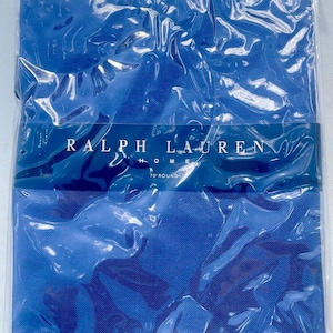 May include: A new, packaged blue tablecloth with the text "RALPH LAUREN HOME" and "70" ROUND" printed on the packaging. The tablecloth is visible through the clear plastic wrapping.