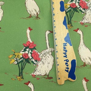 May include: Green fabric with a repeating pattern of white geese with red beaks and feet, interspersed with red and yellow flowers. A wooden ruler with blue accents and the text "Happy Party" is in the image.