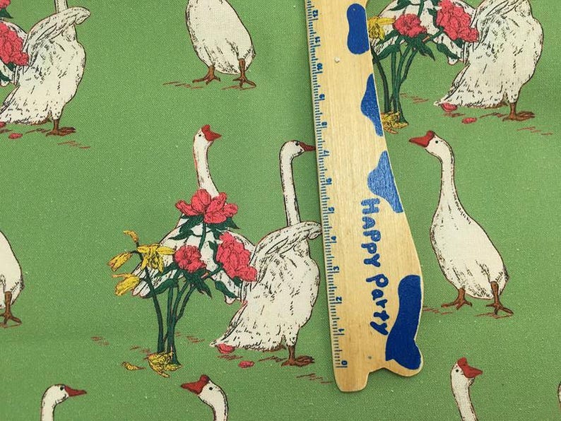 May include: Green fabric with a repeating pattern of white geese with red beaks and feet, interspersed with red and yellow flowers. A wooden ruler with blue accents and the text "Happy Party" is in the image.