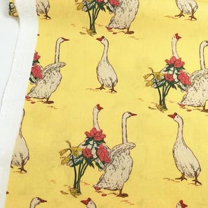 May include: Yellow fabric with a repeating pattern of white geese with red beaks and feet. Some geese are near red and pink floral arrangements. The fabric has a white border on the left side.