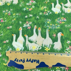 May include: Fabric with a green background featuring white geese with orange beaks and feet, amidst colorful flowers. A wooden ruler with the text "Happy Party" is at the bottom. The fabric is likely cotton or a similar material.