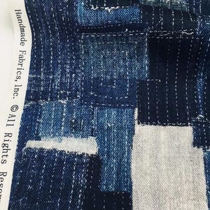 Könnte beinhalten: Nahaufnahme eines Stoffes mit einem Patchwork-Design in Blau- und Weißtönen. Der Stoff weist sichtbare Nähte und den Text "Handmade Fabrics, Inc. © All Rights Reserved." auf.