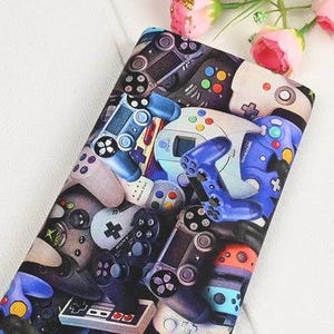Könnte beinhalten: Stoff mit einem Muster aus bunten Videospiel-Controllern. Das Design zeigt Controller in Blau, Grau und Orange mit verschiedenen Tastenanordnungen. Geeignet für Bastel- oder Nähprojekte, ideal für Gamer.
