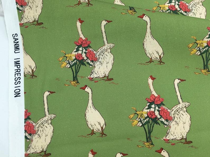 May include: Green fabric with a repeating pattern of white geese with red beaks and floral arrangements. The geese are interspersed with bouquets of red flowers and yellow accents. The text "SANMU IMPRESSION" is printed vertically on the left side.