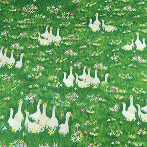 May include: A green fabric with a repeating pattern of white geese and colorful flowers. The geese are clustered in groups, and the flowers are scattered throughout the green background.