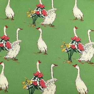 May include: A repeating pattern on a green background features white geese with red beaks and feet. Some geese are adorned with red flowers and yellow foliage. The design has a vintage, illustrated style.