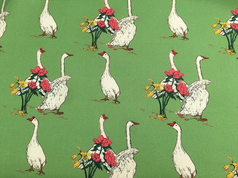 May include: A repeating pattern on a green background features white geese with red beaks and feet. Some geese are adorned with red flowers and yellow foliage. The design has a vintage, illustrated style.