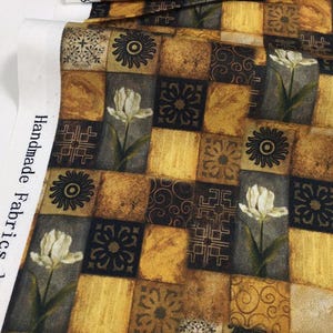 Könnte beinhalten: Stoff mit einem Patchwork-Design mit Quadraten in Gold-, Braun- und Schwarztönen. Die Quadrate sind mit floralen und geometrischen Mustern sowie Illustrationen weißer Tulpen verziert. Der Stoff ist mit "Handmade Fabrics, Inc." beschriftet.