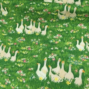 May include: Green fabric with a pattern of white geese and colorful wildflowers. The geese are depicted in various poses, scattered across a field of green grass. The fabric has a whimsical, pastoral theme.