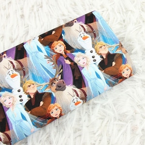 Op de afbeelding: Stof met personages uit de animatiefilm "Frozen". Het ontwerp bevat Elsa, Anna, Kristoff, Olaf en Sven. De stof heeft een herhalend patroon met een mix van kleuren, waaronder blauw, paars, bruin en wit.