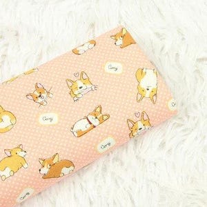 Peut inclure: Tissu rose orné d'un motif répété de corgis de dessin animé dans diverses poses. Les corgis sont représentés dans des tons de marron, blanc et beige, avec des cœurs et le mot "Corgi" dans des bulles. Le tissu a un fond à pois.