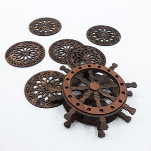 May include: A set of dark brown wooden coasters featuring intricate laser-cut floral patterns, accompanied by a coaster holder designed to resemble a ship's steering wheel with a lighter brown outer ring and dark brown spokes and base.