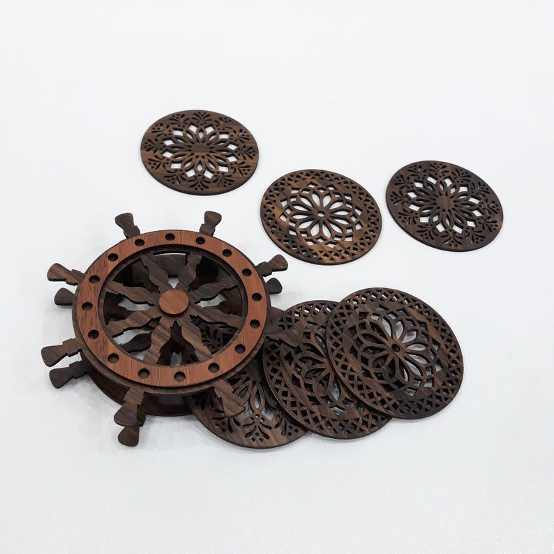May include: A set of dark brown wooden coasters featuring intricate laser-cut floral patterns, accompanied by a circular wooden holder designed to resemble a ship's steering wheel with multiple spokes extending from the outer rim.