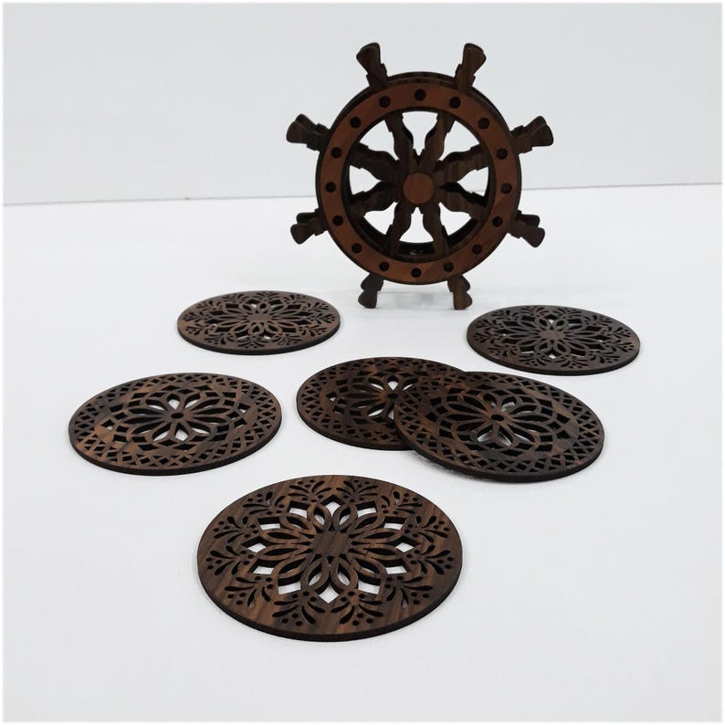 May include: A set of six circular dark brown wooden coasters featuring intricate laser-cut floral patterns, accompanied by a matching dark brown wooden holder shaped like a ship's steering wheel with eight spokes for storage and display.