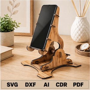 May include: A brown wooden phone stand with a visible grain pattern, featuring an adjustable angled support structure and a base with four feet. The stand holds a black smartphone. The text SVG, DXF, AI, CDR, PDF is printed at the bottom.