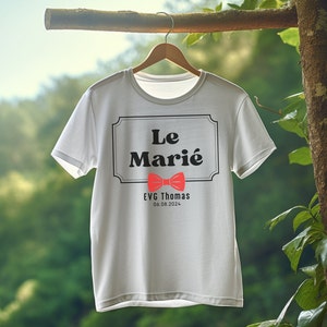 K&ouml;nnte beinhalten: Wei&szlig;es T-Shirt mit schwarzem Text, der "Le Mari&eacute;" in einem dekorativen Rahmen lautet. Unter dem Text befindet sich eine rote Fliege. Der Text "EVG Thomas 06.08.2024" befindet sich unter der Fliege.
