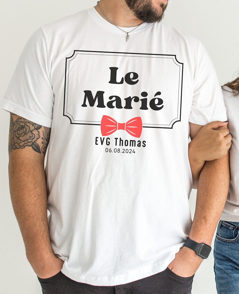 K&ouml;nnte beinhalten: Wei&szlig;es T-Shirt mit einem schwarz-wei&szlig;en Etikett, auf dem "Le Mari&eacute;" steht, darunter ein roter Fliege. Das Etikett enth&auml;lt auch den Text "EVG Thomas 06.08.2024".