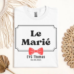 K&ouml;nnte beinhalten: Wei&szlig;es T-Shirt mit einem schwarz-wei&szlig;en Etikett, auf dem "Le Mari&eacute;" mit einer roten Fliege und dem Text "EVG Thomas 06.08.2024" darunter steht.