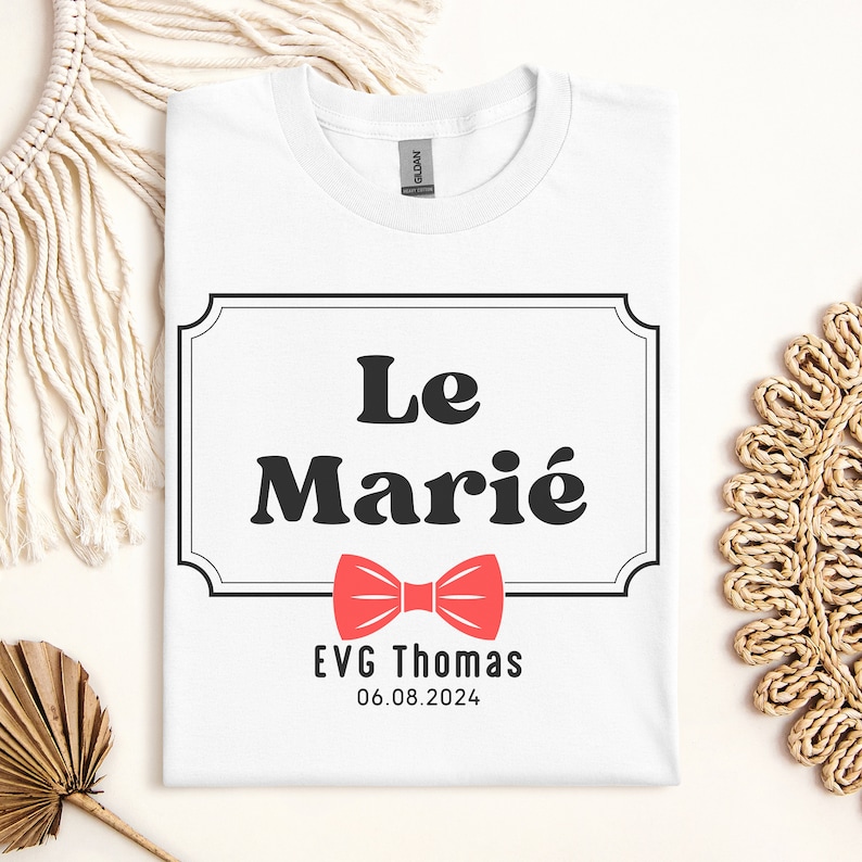 K&ouml;nnte beinhalten: Wei&szlig;es T-Shirt mit einem schwarz-wei&szlig;en Etikett, auf dem "Le Mari&eacute;" mit einer roten Fliege und dem Text "EVG Thomas 06.08.2024" darunter steht.