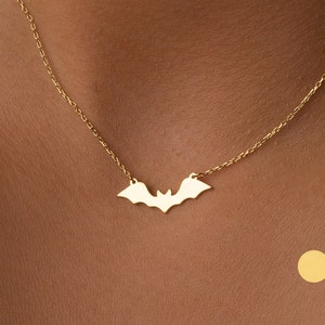 May include: A gold chain necklace with a bat pendant. The bat is a simple silhouette with no details. The necklace is on a model's neck.