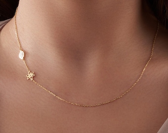 May include: A delicate gold chain necklace with two small flower-shaped pendants. The necklace is on a model's neck.