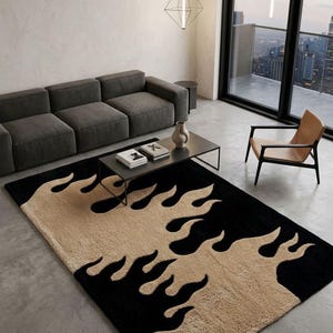 Könnte beinhalten: Rechteckiger Teppich mit schwarzem Hintergrund und beigefarbenen flammenartigen Formen. Der Teppich befindet sich in einem modernen Wohnzimmer mit grauem Sofa, schwarzem Couchtisch und einem großen Fenster mit Blick auf die Stadt. Ca. 200 cm x 300 cm.
