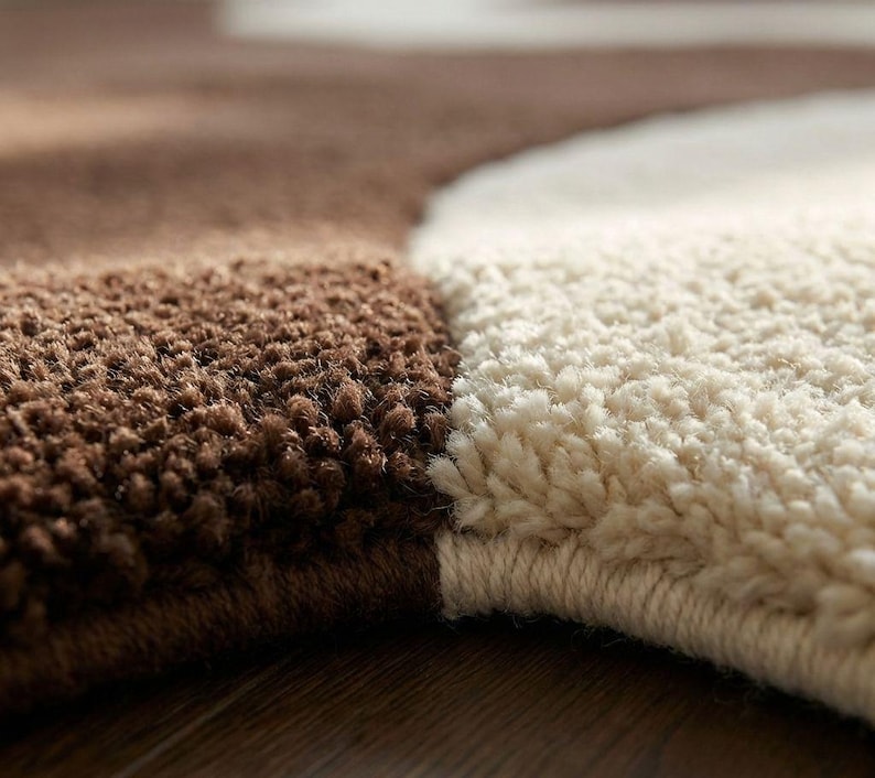 May include: Close-up of a brown and cream-colored rug. The rug has a textured, plush surface with a distinct color block design. The brown section is a darker shade, while the cream section is lighter. The rug appears to be made of soft material.