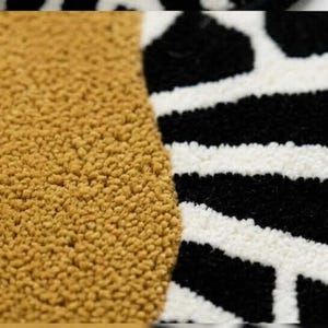 Könnte beinhalten: Nahaufnahme eines strukturierten Teppichs mit geometrischem Design. Der Teppich hat einen senfgelben Abschnitt und einen Abschnitt mit einem schwarz-weißen Muster. Die Textur des Teppichs ist sichtbar und zeigt seinen weichen, geschlungenen Flor.