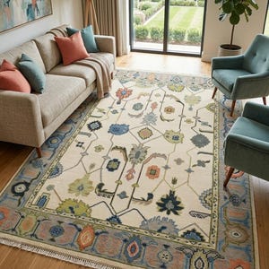 Könnte beinhalten: Ein rechteckiger Teppich mit cremefarbenem Grund und einem symmetrischen Muster aus floralen und geometrischen Motiven in Blau-, Grün-, Orange- und Brauntönen. Der Teppich hat eine breite Zierbordüre und kurze weiße Fransen an den Enden.