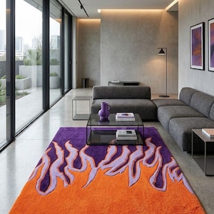 Könnte beinhalten: Ein rechteckiger Teppich mit einem Flammenmuster in Orange, Lila und Helllila. Der Teppich liegt in einem modernen Wohnzimmer mit grauen Möbeln und großen Fenstern. Die Farbgebung und das Design schaffen eine moderne Atmosphäre.