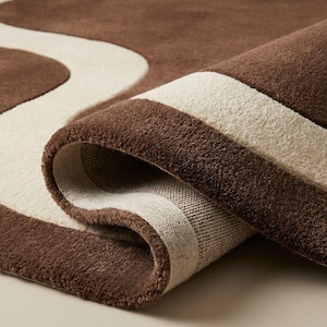 May include: A rolled-up brown and cream-colored rug. The rug features a wavy cream design against a brown background. The edges are also brown, creating a border. The rug is made of a soft, plush material.