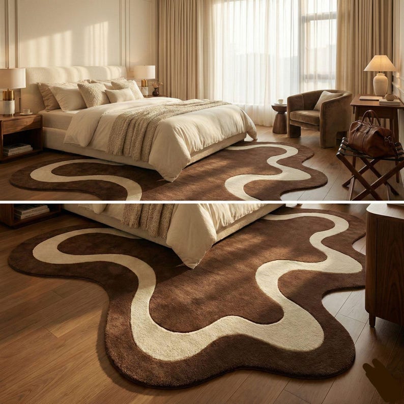 May include: A brown and cream-colored area rug with a unique, flowing design in a bedroom setting. The rug's pattern resembles a meandering river or abstract shape, adding a touch of modern flair to the room's decor. The rug is placed in front of a bed.