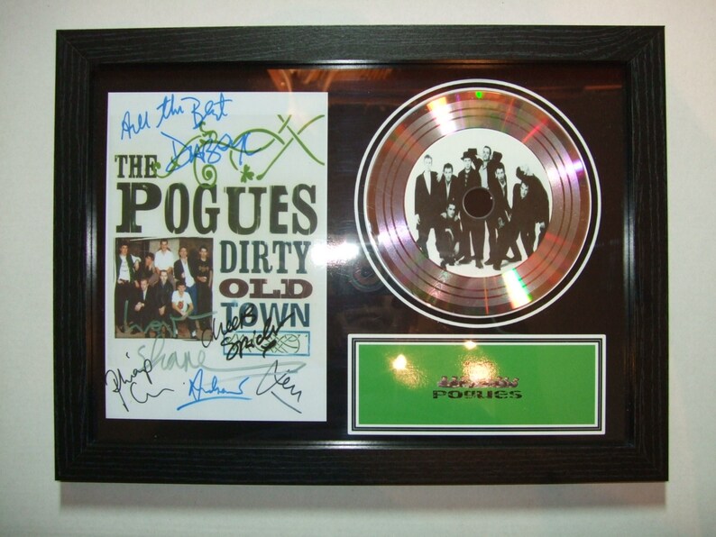 May include: A framed platinum record for The Pogues' album "Dirty Old Town". The record is surrounded by a black frame and a white mat. The album cover is visible in the frame, along with signatures from the band members. The record is a silver disc with a holographic effect.