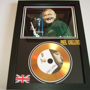 Peut inclure: Un disque d'or encadré avec une photo de Phil Collins et le texte "Phil Collins" sur la plaque. Le disque est un disque d'or avec une photo de Phil Collins dessus.