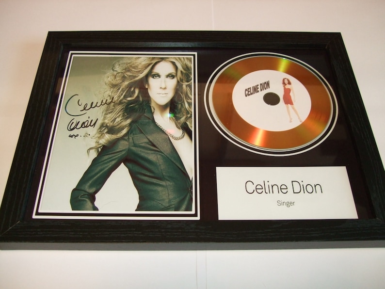 Może przedstawiać: Złota płyta w ramie z fotografią Celine Dion i jej podpisem. Płyta jest ozdobiona napisem "Celine Dion" i tekstem "Singer".