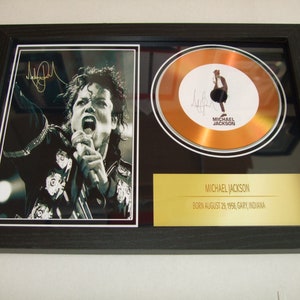 Puede incluir: Un disco de oro enmarcado con una foto en blanco y negro de Michael Jackson cantando en un micrófono. El disco tiene un fondo dorado con una silueta negra de Michael Jackson. El marco tiene una placa dorada con el texto "MICHAEL JACKSON NACIDO EL 29 DE AGOSTO DE 1958, GARY, INDIANA."
