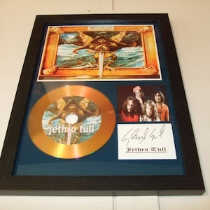 Könnte beinhalten: Eine gerahmte goldene CD mit einem Bild der Band Jethro Tull auf der Vorderseite. Die CD ist von den Bandmitgliedern signiert. Der Rahmen ist schwarz mit einer blauen Passepartout.
