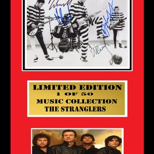 Puede incluir: Una fotografía en blanco y negro de los miembros de la banda The Stranglers con uniformes de prisión, sosteniendo instrumentos musicales. La foto está firmada por cada miembro de la banda. La foto está enmarcada con una placa dorada que dice "Edición limitada 1 de 50 Colección musical The Stranglers". Debajo de la foto enmarcada hay una foto más reciente de los miembros de la banda.
