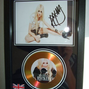 May include: A framed gold record with a black and white photo of a woman with long blonde hair. The record is titled "The Pretty Reckless" and the album title is "Tonight". The record is signed with a black marker.