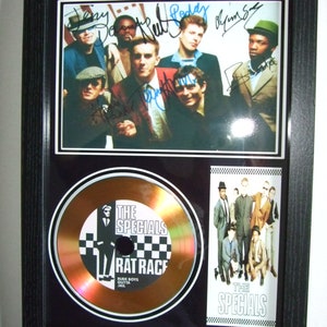 Op de afbeelding: Een ingelijste gouden plaat met een zwart-wit afbeelding van de band The Specials en de albumtitel "Rat Race". De plaat is gesigneerd door de bandleden: Jerry Dammers, Neville Staple, Terry Hall, John Bradbury en Lynval Golding.