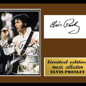 Puede incluir: Una fotografía en blanco y negro de Elvis Presley actuando en un escenario. Lleva un mono blanco con un diseño de lentejuelas y una correa de guitarra negra. Sostiene un micrófono en su mano derecha y una guitarra en su mano izquierda. La foto está enmarcada en un marco marrón con una placa dorada que dice "edición limitada colección musical ELVIS PRESLEY".
