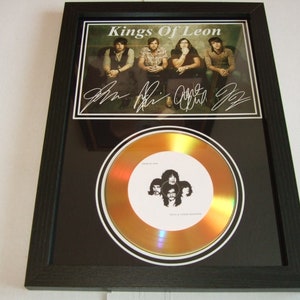 May include: A framed gold record award with a black background and a photo of the band Kings of Leon. The record is signed by all four band members. The text "Kings of Leon" is printed in white on a black background.
