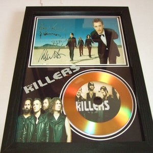 Puede incluir: Un disco de oro enmarcado para The Killers. El disco está rodeado por un borde negro con el nombre de la banda en letras blancas. El nombre de la banda también está impreso en el propio disco. Una foto en blanco y negro de la banda está en la mitad superior del marco. La foto está firmada por los miembros de la banda.