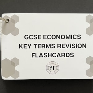 May include: White flashcards with a black ring binder. The flashcards have a grey hexagonal pattern on the edges and the text "GCSE ECONOMICS KEY TERMS REVISION FLASHCARDS (YF) REVISION" in black.