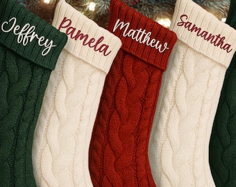 May include: Five cable-knit Christmas stockings in varying colors hang in front of a fireplace. The stockings are green, cream, and red, each with a name embroidered on the cuff: "Jeffrey", "Pamela", "Matthew", "Samantha", and "Eric".